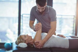 Physical therapist guiding a patient through a gentle leg movement in a treatment room.