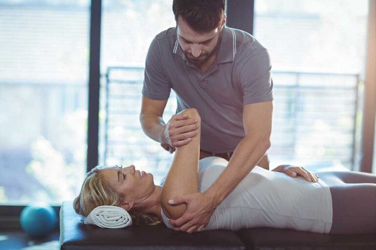 Physical therapist guiding a patient through a gentle leg movement in a treatment room.
